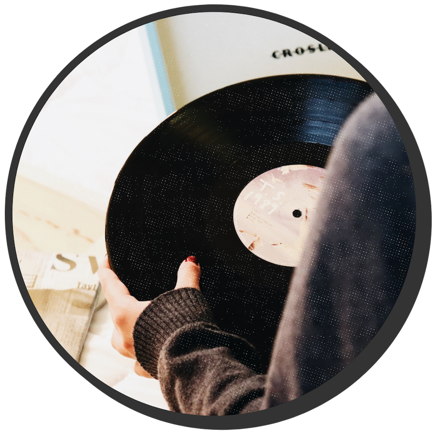 Looking over the shoulder of a person holding a record in two hands. They are about to put it on the record player to listen.