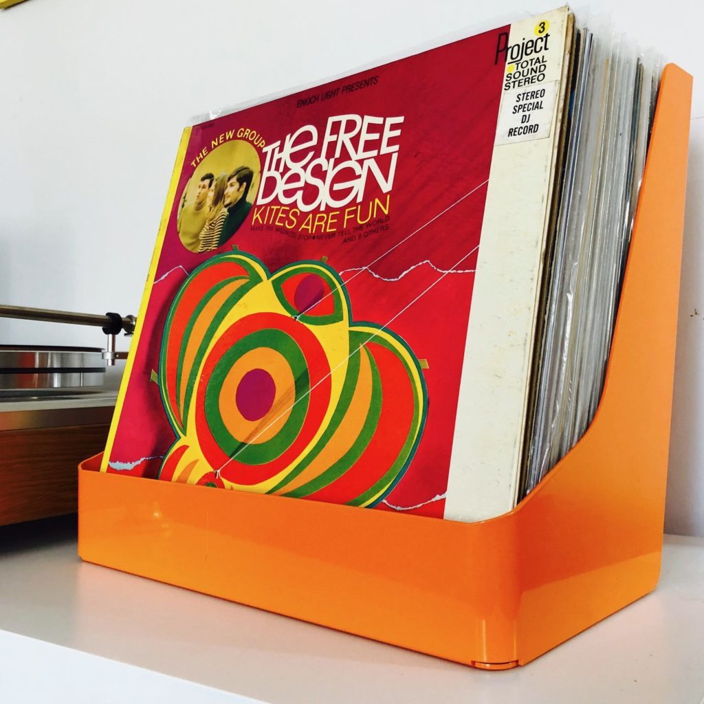 An orange plastic bin sitting on a table holding about 20 colorful records