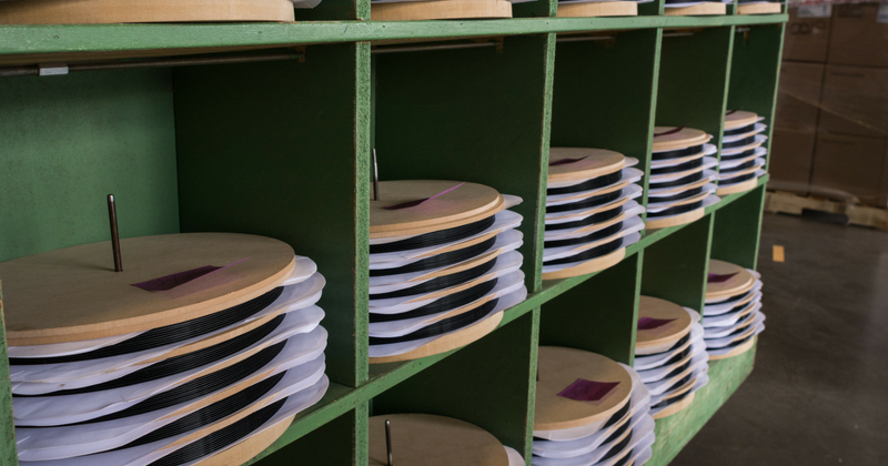 shelves in a vinyl manufacturing plant holding multiple LP records separated by wood and paper