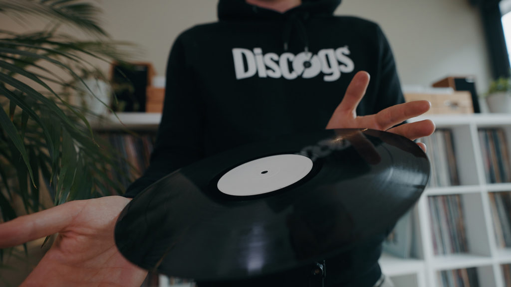 person with a discogs hoodie inspecting a vinyl record for dirt