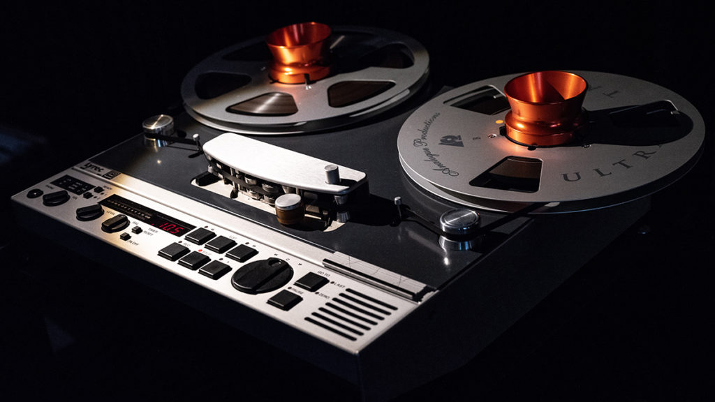 A partially shadowed image of a reel to reel tape recorder with reels loaded.