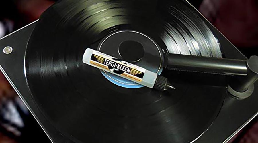 a bottle of tergikleen cleaner on top of a black vinyl record sitting on a vacuum record cleaner