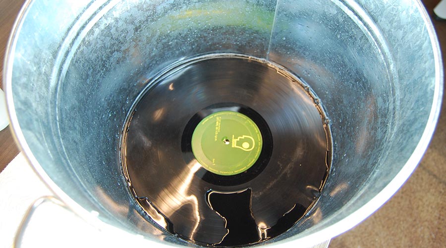 Black vinyl record in a tin bucket soaking in cleaning solution